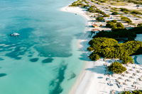 Drone view of a tropical coastline with turquoise water, white sand beach, and beach umbrellas lining the shore.