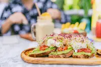 Avocado toast with poached eggs and microgreens served on a wooden board at Coco Café, with a smoothie in the background