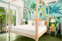 Four-poster bed in Deluxe Coco Casita at Boardwalk Boutique Hotel Aruba, with colorful jungle wall mural.