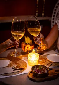 Two people clink chilled white wine glasses over a candlelit dinner table.