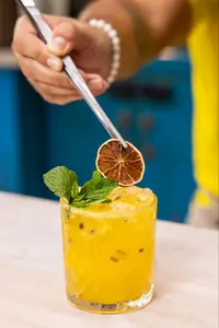 Hand garnishing yellow citrus cocktail with dried lime slice and fresh mint.