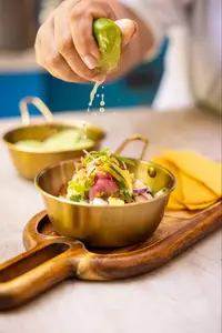 Hand squeezing lime over colorful ceviche in a golden bowl on wooden serving board.