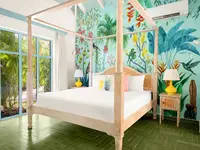 Four-poster bed in Deluxe Coco Casita at Boardwalk Boutique Hotel Aruba, with colorful jungle wall mural.