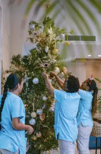 Boardwalk Boutique Hotel Aruba team decorating the lobby Christmas tree with ornaments and lights, creating a festive holiday welcome.