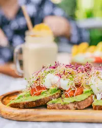 Avocado toast with poached eggs and microgreens served on a wooden board at Coco Café, with a smoothie in the background